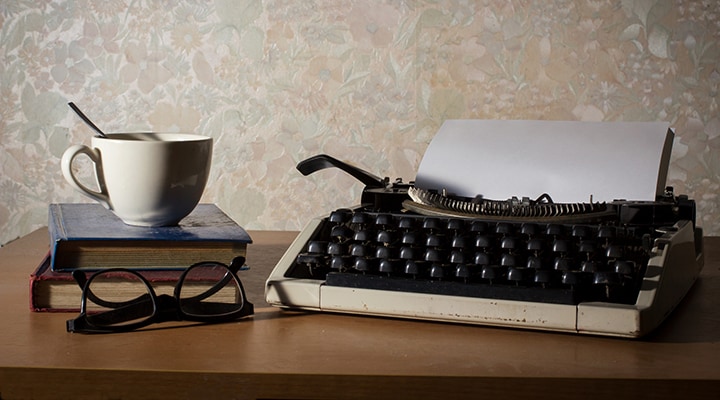 A coffee cup, book, eyeglasses and vintage typewriter