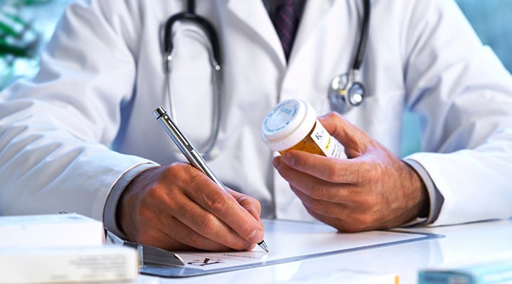 Health care provider writing a prescription for medication while holding a pill bottle.