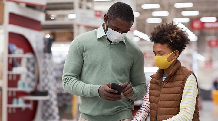Father and daughter in store wearing masks and looking at smart phone