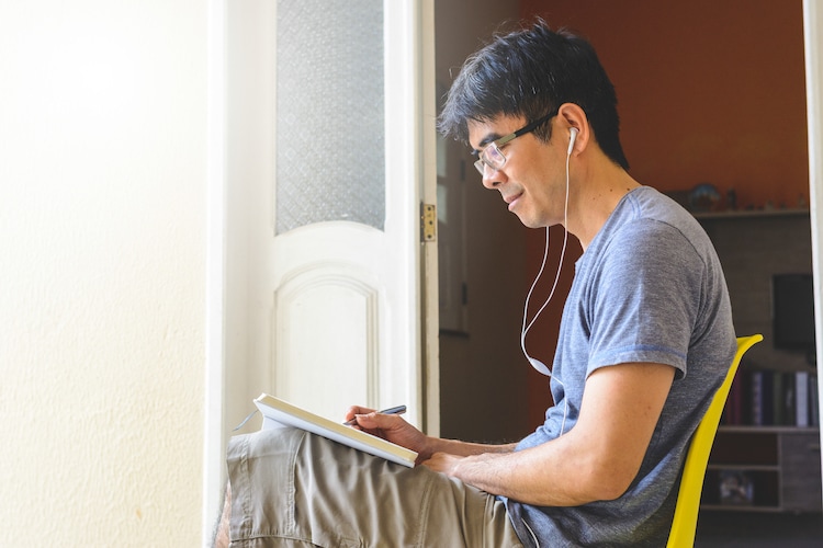 Asian man sitting with a book and headphones