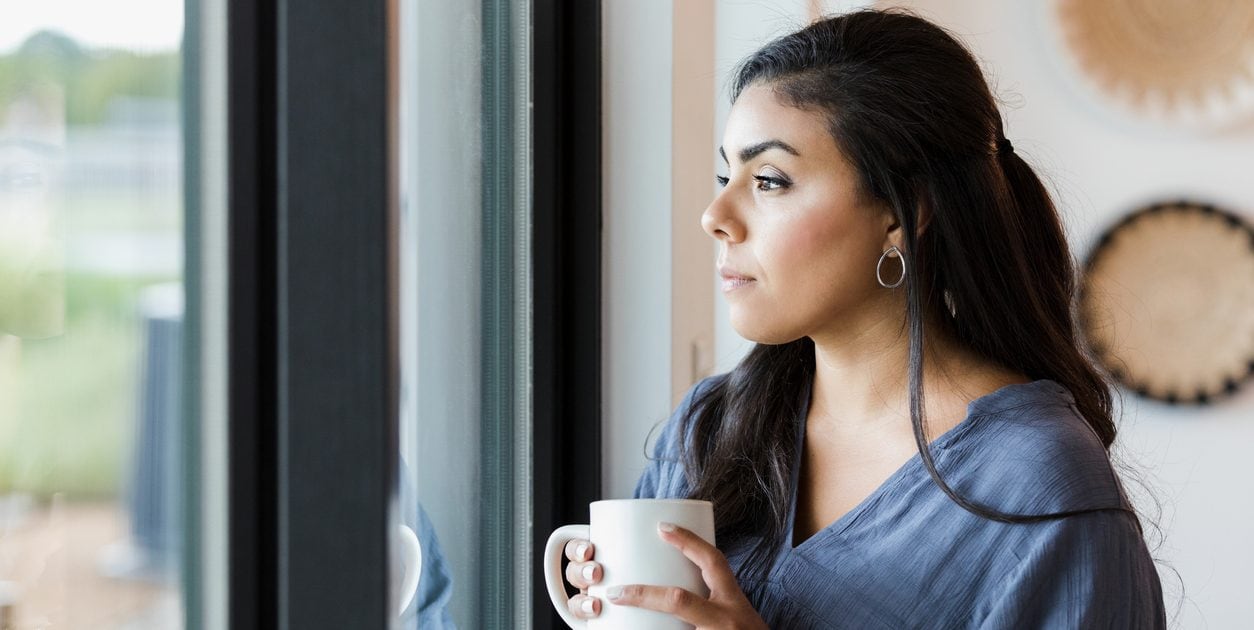 Mid adult woman stands at window with hot drink