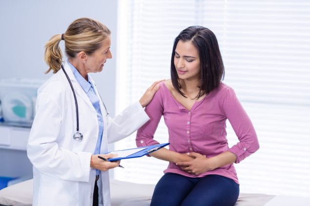 Woman holding her stomach in pain talking to doctor.