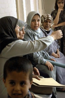 Women waiting on a bench at Al-Arafa clinic. Child appears in front of the shot