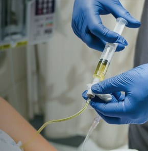 Closeup of hands wearing medical gloves giving IV injection.
