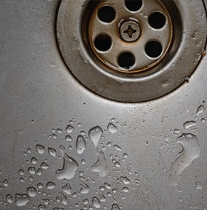 Closeup of sink drain with water drops.