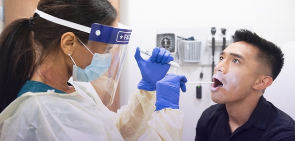 healthcare worker donning full personal protective equipment (PPE) examining a patient