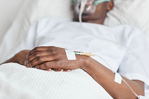 Closeup of patient wearing medical gown in bed with IV in hand.
