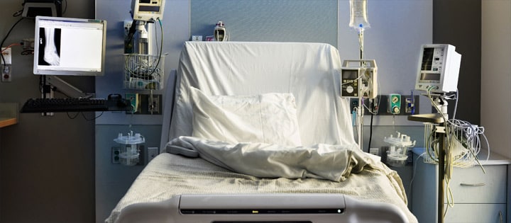 Empty hospital bed with covers open, surrounded by healthcare devices