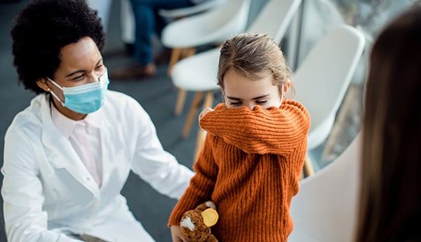 Healthcare worker with a mask, triaging a coughing child in a healthcare facility waiting room.