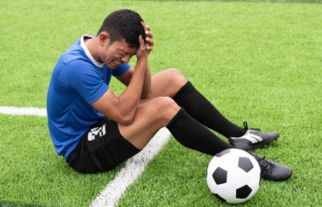 Image of a soccer player holding his head with an expression of pain on his face