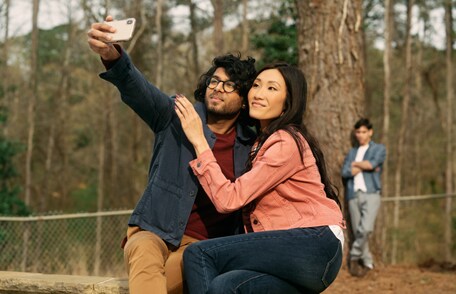 Image of a young couple taking a selfie while a young man watches in the background