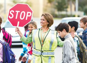 Woman crossing guard holding stop sign while school children pass by.
