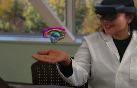 Woman uses augmented reality headset to visualize a human brain cutaway in the palm of her hand