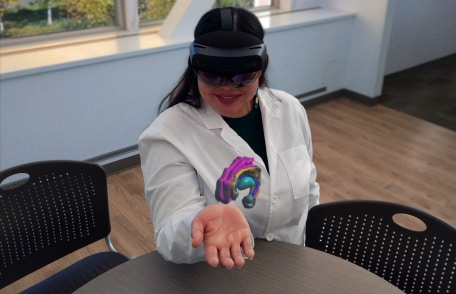 A different angle of a woman using an augmented reality headset to visualize a human brain cutaway in the palm of her hand