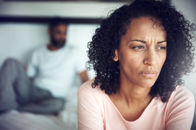 Shot of a mature woman looking sad while her husband sits in the background.