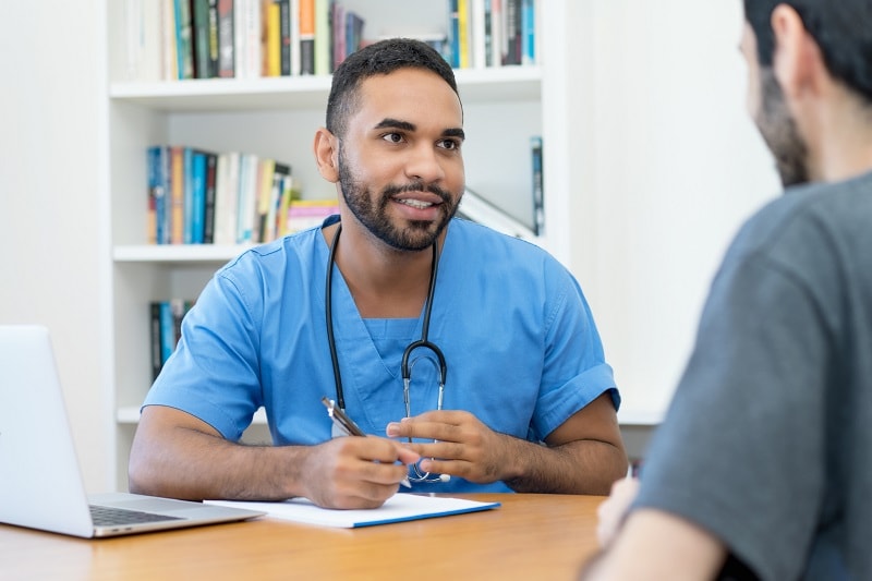 Young Hispanic male doctor talking with male patient.