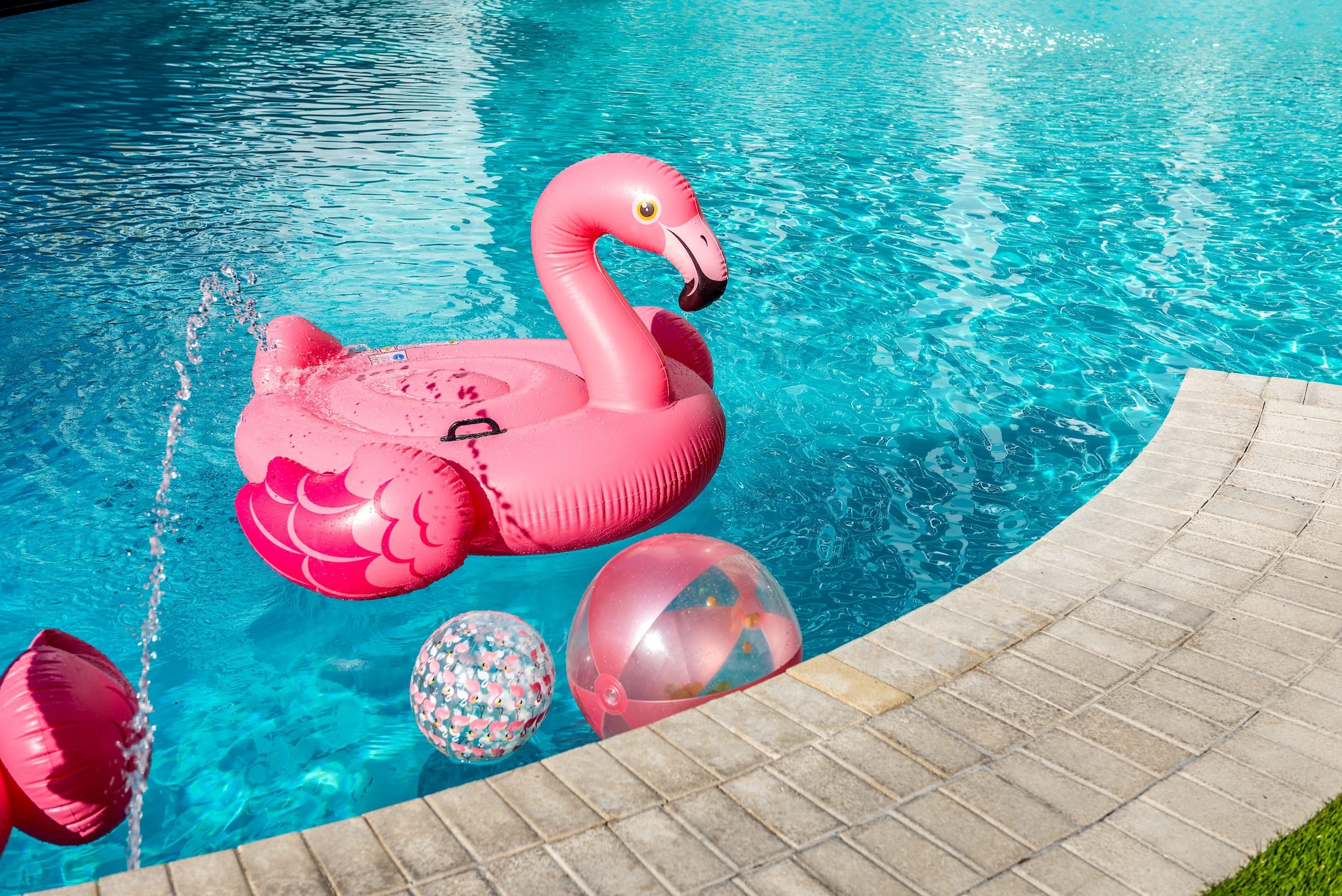 A flamingo pool float in a pool with other pool toys.
