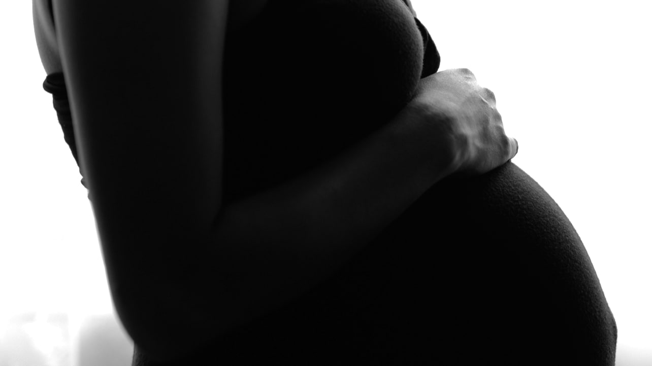 Black and white photo of a pregnant woman holding her belly.