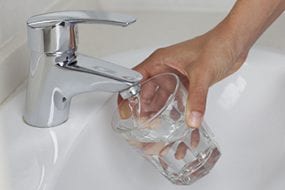 Hand filling a glass up with water at the sink.