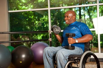 Man in a wheel chair lifting weights in a gym.