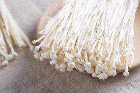 Enoki mushrooms are white, with long stems and small caps.