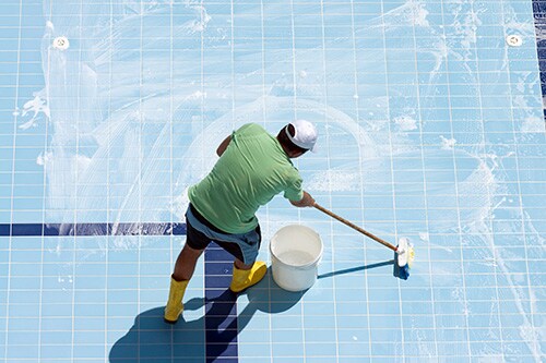 Man cleaning the tiled floor of swimming-pool