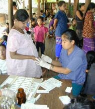 Pregnant woman having a fingerprick performed by a health worker for diagnosis of malaria in a semi-open clinic