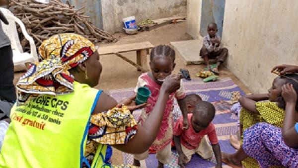 Community health worker administering preventative antimalarial medication to young children.