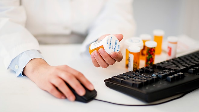 Pharmacist with various medication bottles working at computer.