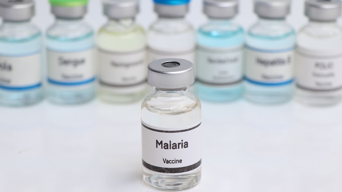 Malaria vaccine in a vial on a table with seven vials behind.