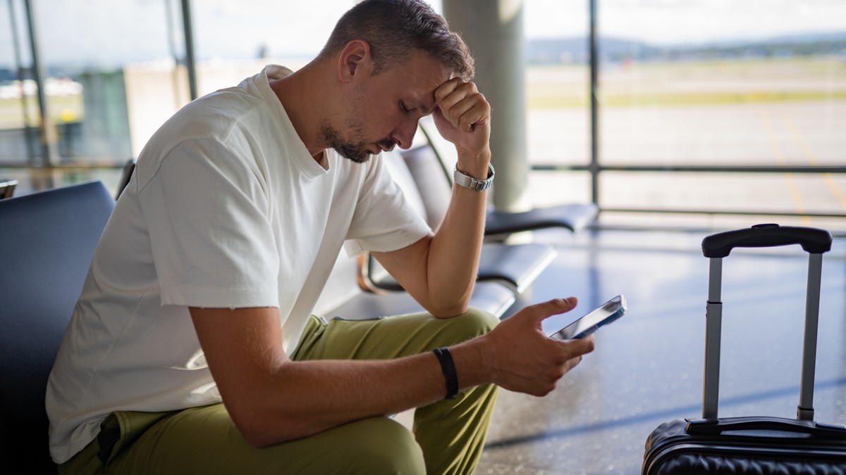 Man feeling ill at airport rests with head on hand.