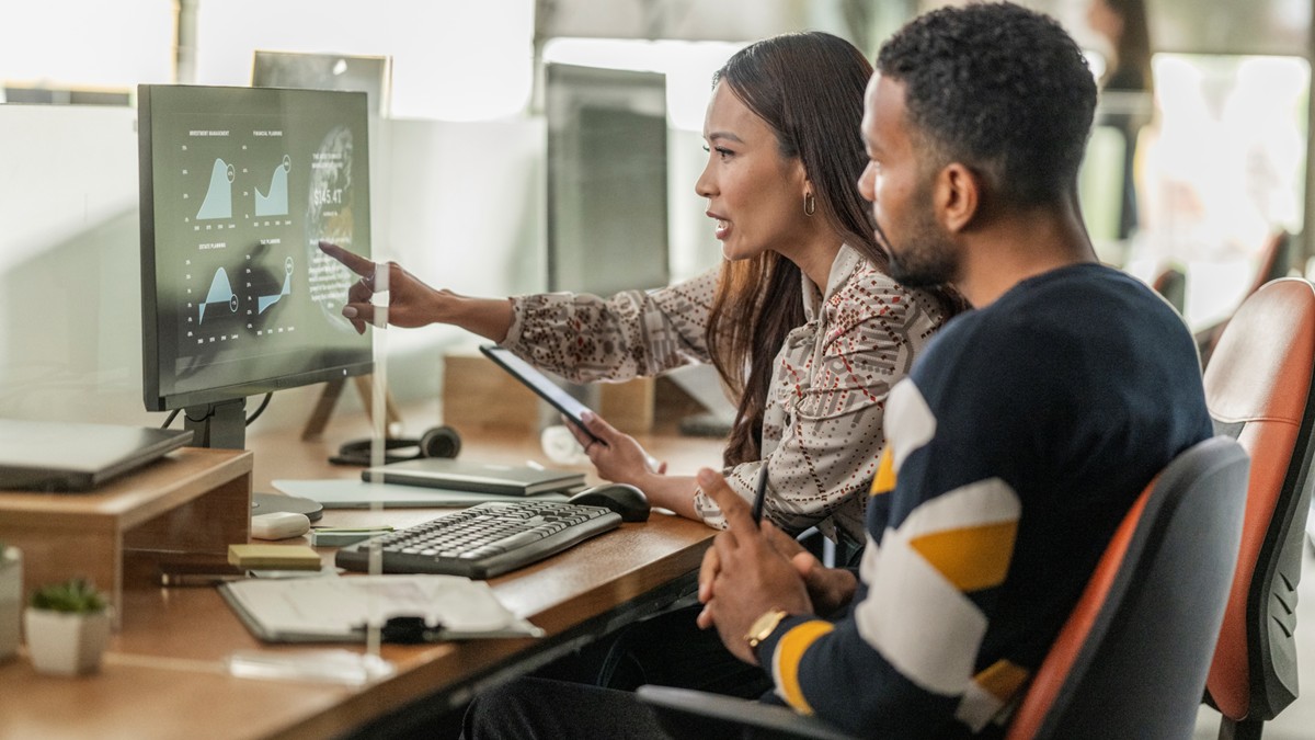 A woman and man analyze data on an office computer.