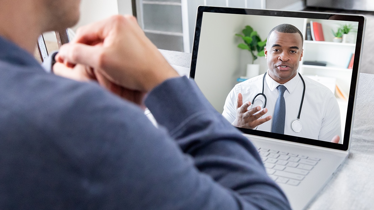 Patient sitting at table while on video conference call with Doctor.