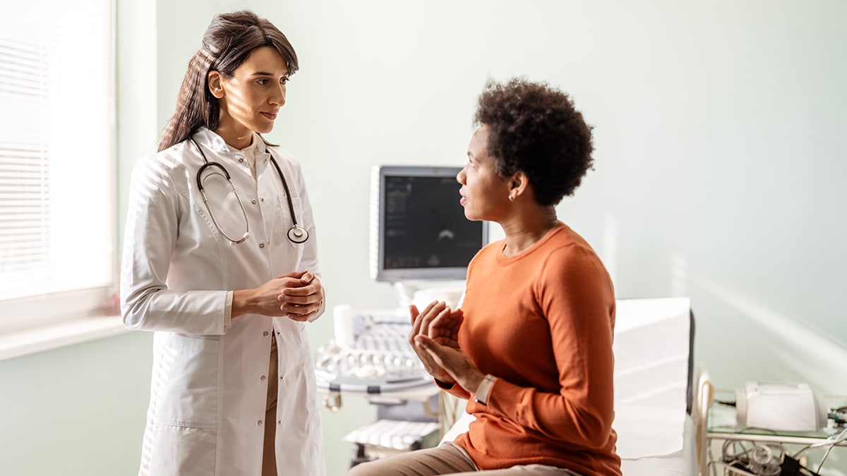A female doctor talks with her patient in front of her as they talk about her concerns. - stock photo
