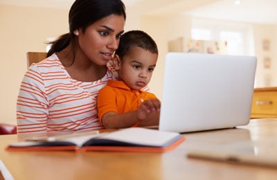 Woman looking at a laptop computer while holding young boy in her lap.