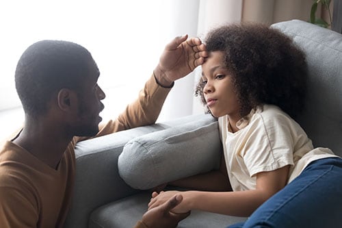 Caring African American father touching forehead of ill kid daughter