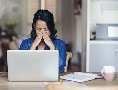 Frustrated young college female with her hands to her face in front of a laptop