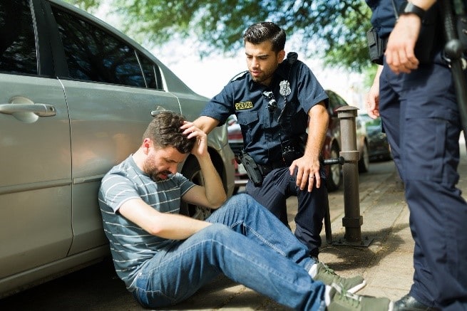 man sitting on ground near police car