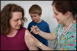 The figure above is a photograph showing a nurse administering a vaccination to a patient, as the patient's son watches.