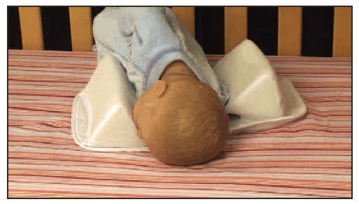 The figure shows a simulated display using a doll in an infant sleep positioner with two bolsters, demonstrating how an infant's face can get trapped against the bolster, causing suffocation.