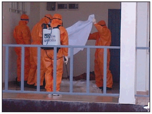 The figure is a photograph of a burial team preparing to wrap a body in a Muslim shroud, illustrating the incorporation of a dignified component of a standard operating procedure for safe, dignified medical burial in Sierra Leone in October 2014.