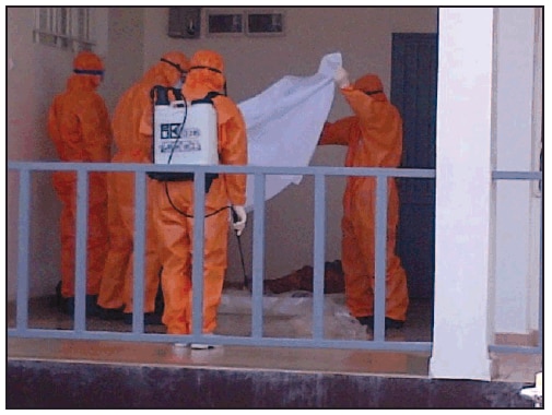 The figure is a photograph of a burial team preparing to wrap a body in a Muslim shroud, illustrating the incorporation of a dignified component of a standard operating procedure for safe, dignified medical burial in Sierra Leone in October 2014. 