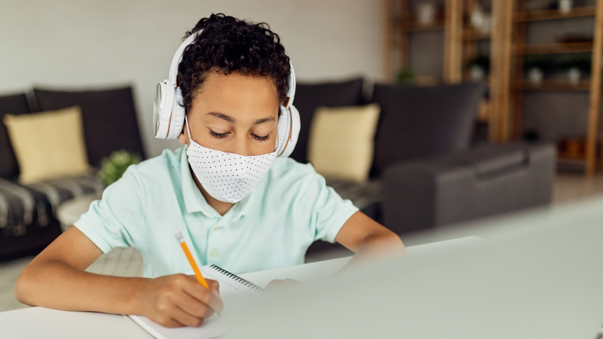 The figure is a photo of a young person wearing a mask while studying at home.
