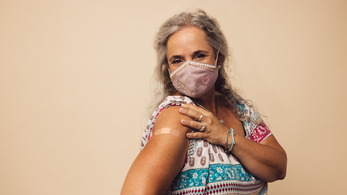 ss7003a1_AdultVaccination_IMAGE_14May21_1200x675 The figure is a photo of a person wearing a mask with a bandage on their arm.