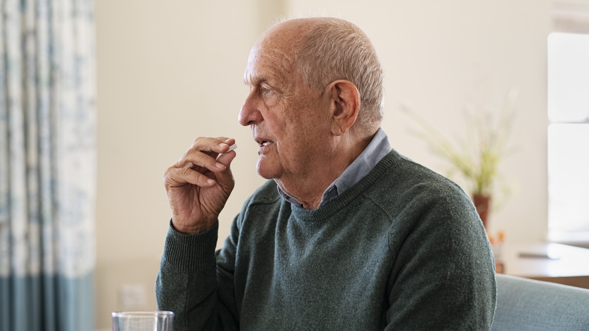 The figure is a photo of an elderly person seated in front of a glass of water preparing to take a pill they are holding.