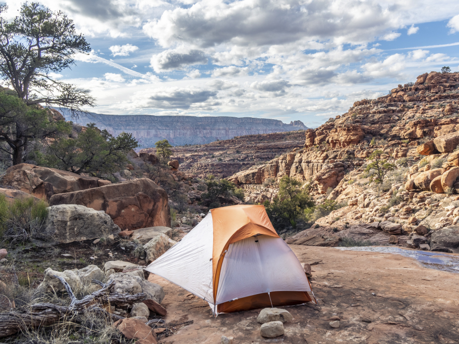 Outbreak of Acute Gastroenteritis Among Rafters and Backpackers in the Backcountry of Grand Canyon National Park, April–June 2022 The figure is a photo of an orange and white tent set up on a flat rock surrounded by a desert environment.