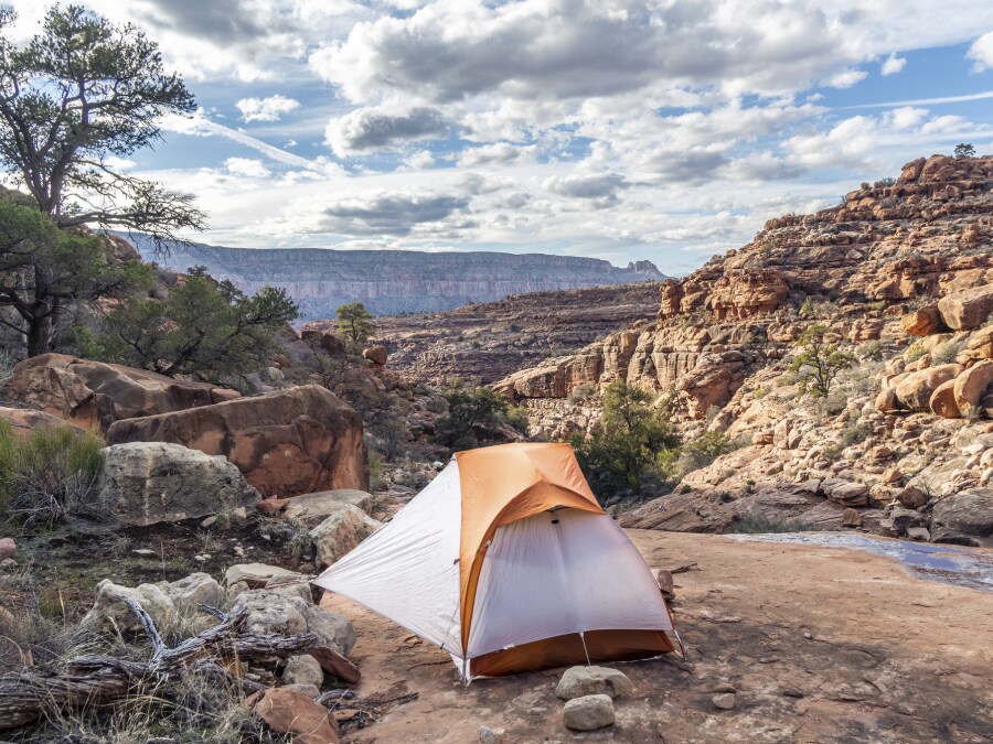 The figure is a photo of an orange and white tent set up on a flat rock surrounded by a desert environment.