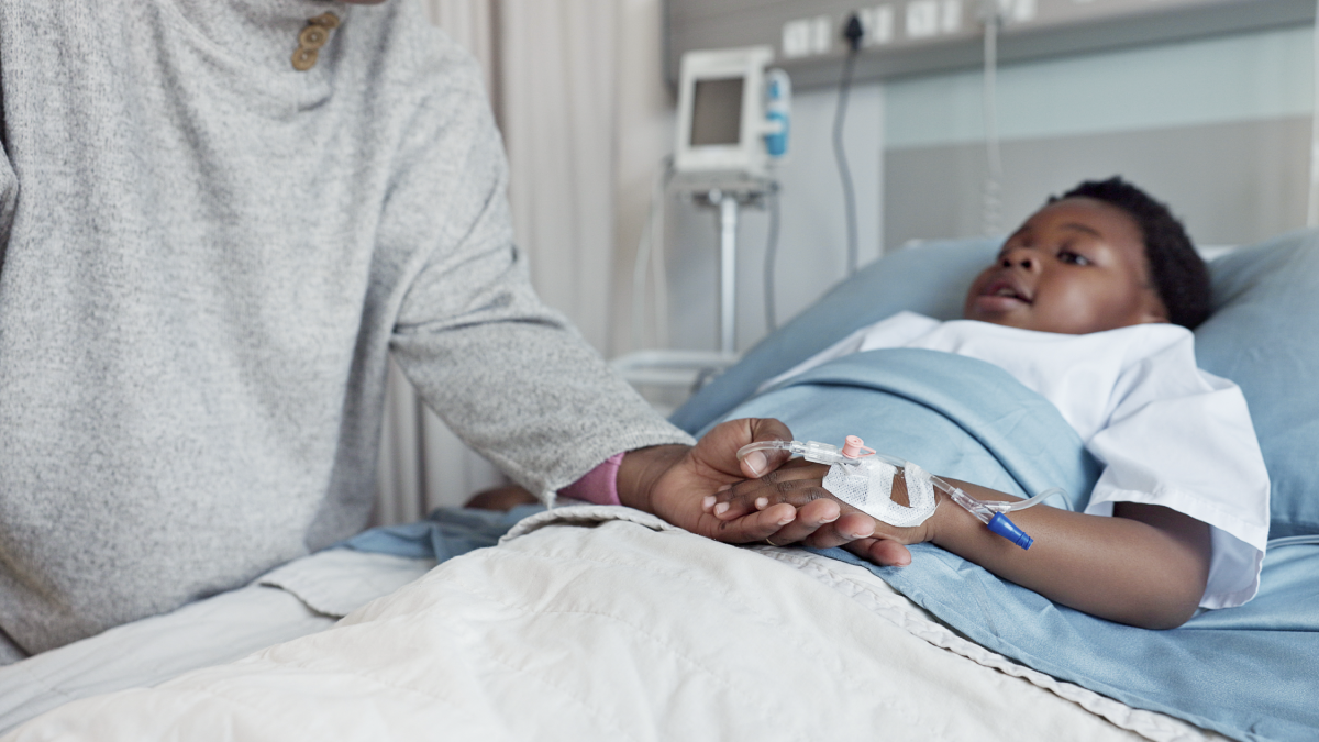 This image shows a child in a hospital bed while their parent holds their hand.
