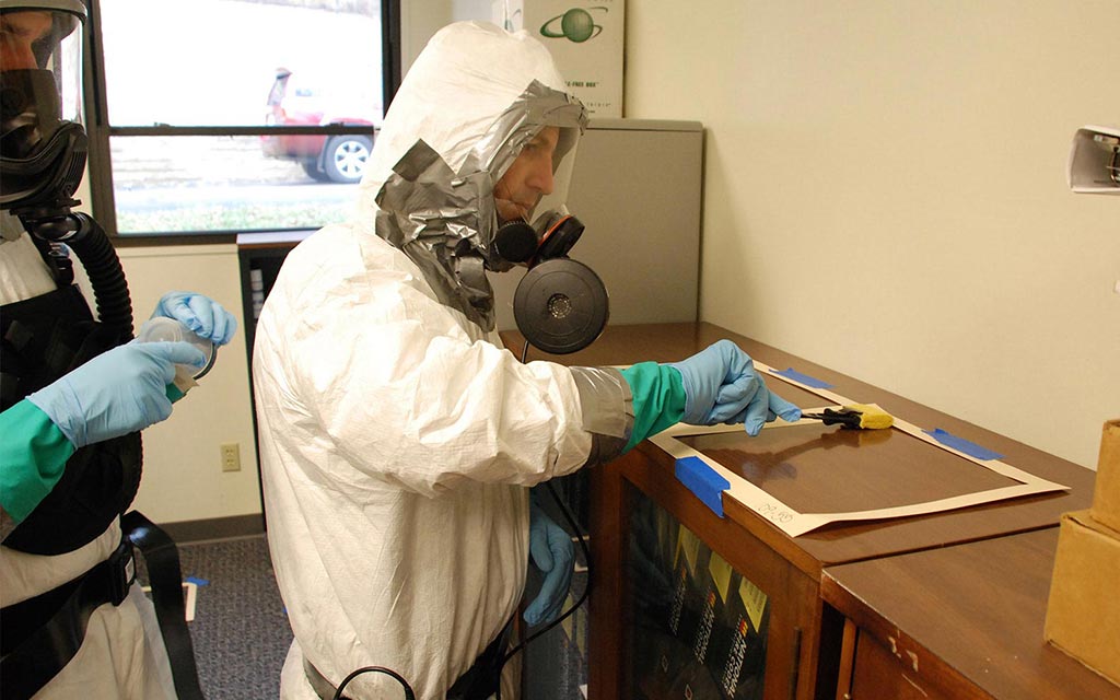 Worker in personal protective equipment (PPE) or hazmat suit checking surfaces for anthrax.