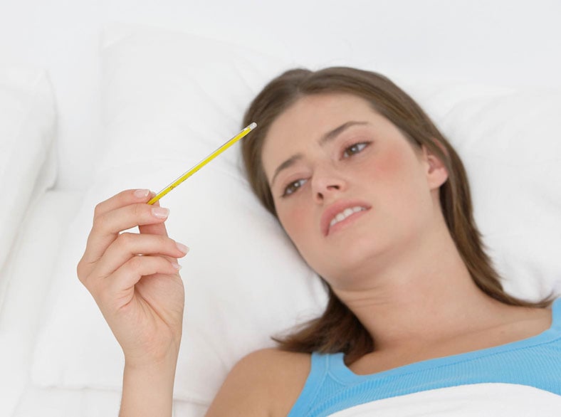 A woman lying in bed checking her temperature.